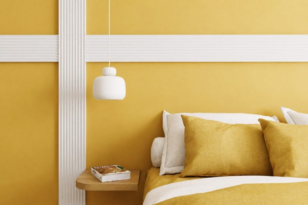 Détail de la tête de lit jaune ocre, soulignée par un décor blanc rainuré et une suspension de chevet.