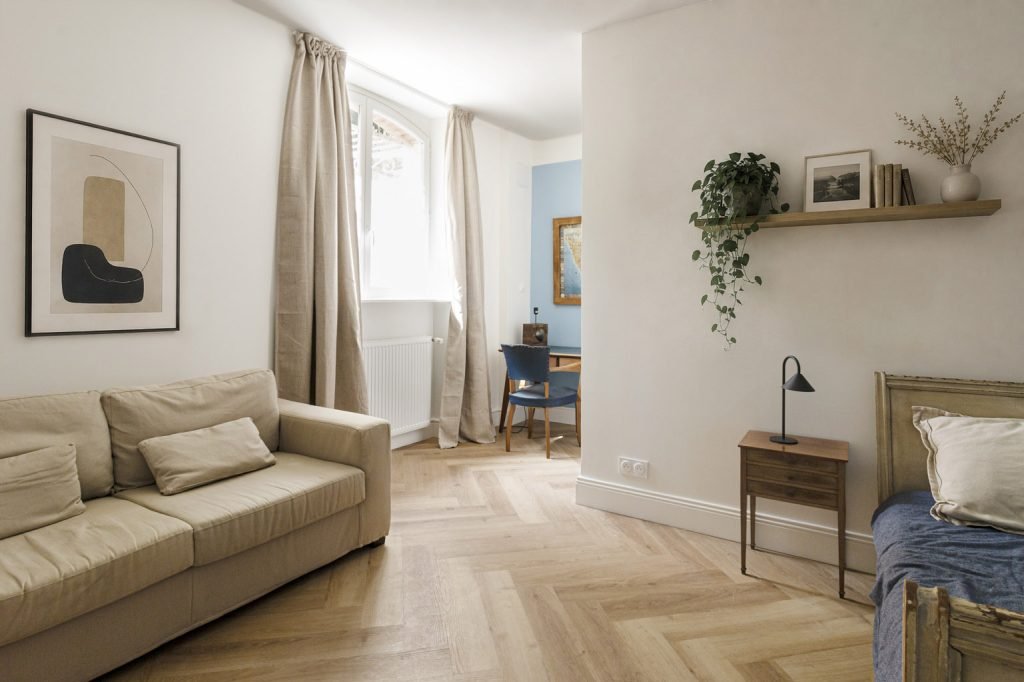 Chambre d’adolescent aux murs blancs et bleus, avec lit simple, canapé beige et coin bureau.