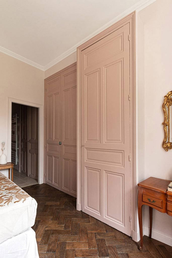 Placards intégrés aux portes moulurées rose poudré dans une chambre parentale avec parquet à bâtons rompus.