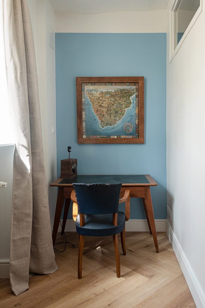 Coin bureau en bois dans une chambre d’adolescent, installé contre un mur bleu et décoré d’une carte encadrée.