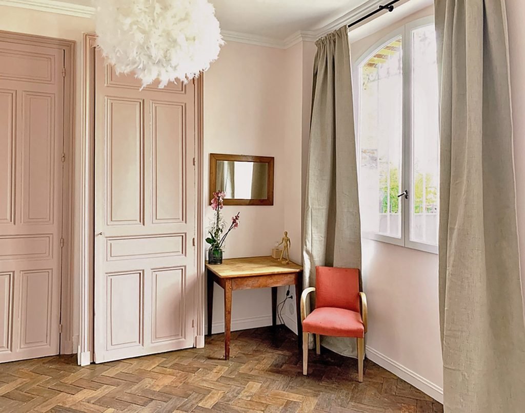 Coin bureau dans une chambre parentale rose poudré, avec parquet à bâtons rompus, portes moulurées et fenêtre cintrée.