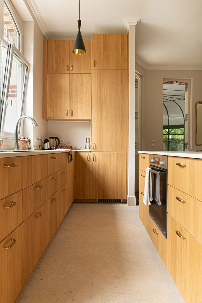Cuisine beige et bois aménagée en longueur, avec façades en chêne, rangements toute hauteur et îlot central parallèle au linéaire.