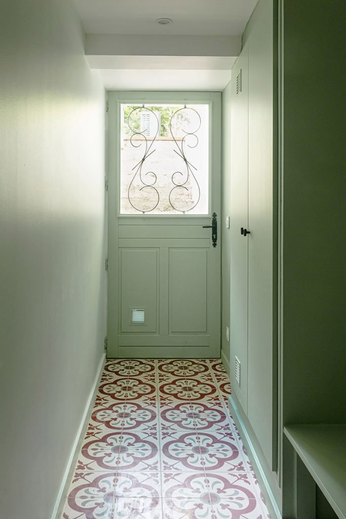 Entrée secondaire du souplex aux murs vert sauge, avec porte vitrée et sol en carreaux de ciment rouges et blancs.