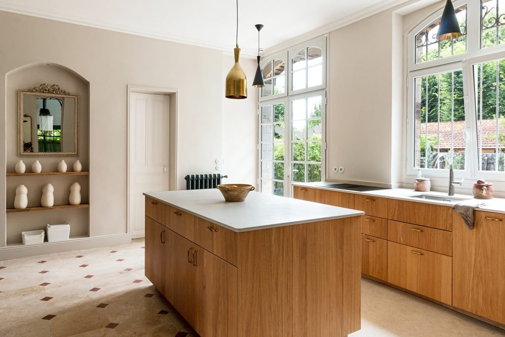 Cuisine rénovée en chêne avec îlot central et sol en travertin dans une maison ancienne à Croissy-sur-Seine.