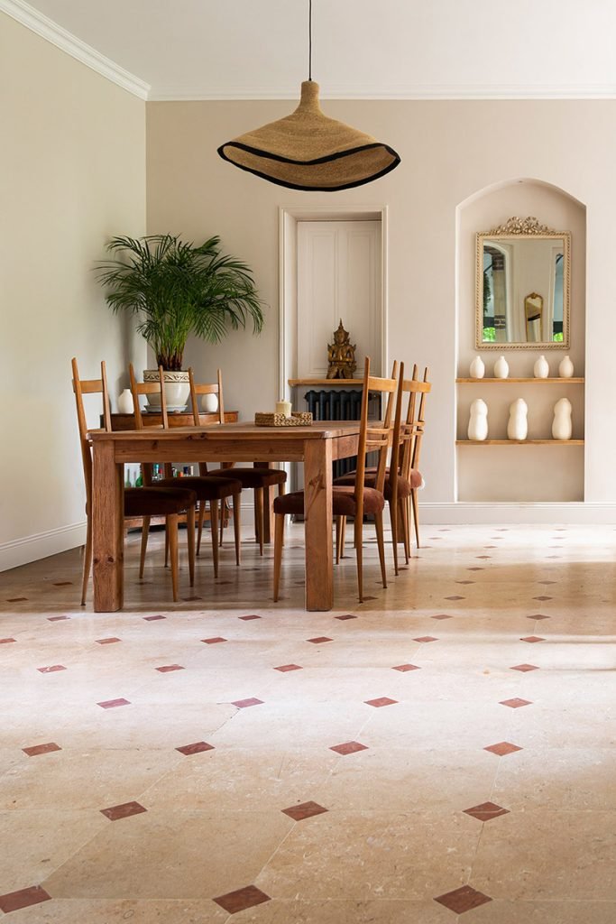 Salle à manger beige et bois avec table ancienne, niches décoratives et sol en travertin à cabochons.