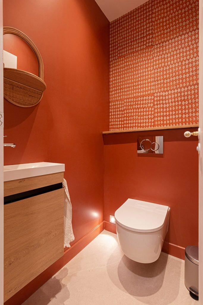 Toilettes rouge terracotta avec WC suspendu, papier peint géométrique et meuble vasque en bois.