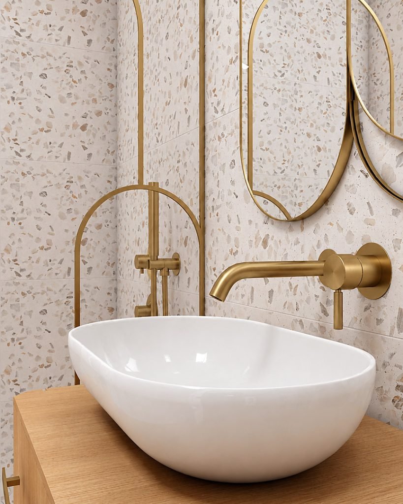 Détail de la vasque blanche posée sur un meuble en bois, avec robinet mural en laiton et carrelage en terrazzo clair.