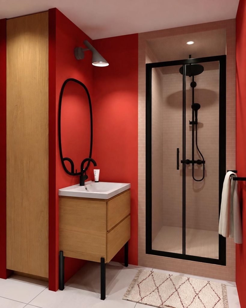 Salle d’eau aux murs rouges avec meuble vasque en bois et douche encadrée de noir.