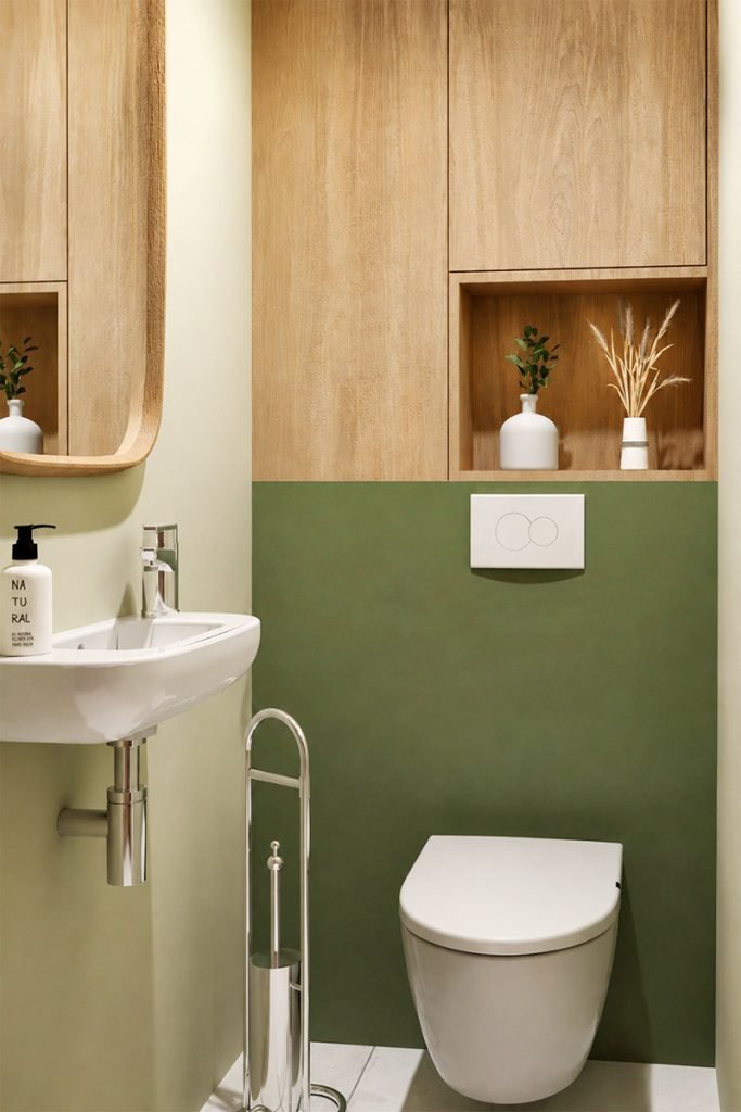 Toilettes aux murs vert olive avec WC suspendu, lave-mains et rangements intégrés en bois.